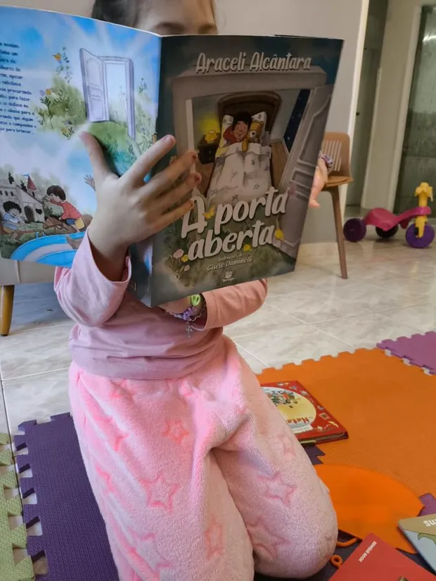Uma das filhas lendo em casa, segurando o livro na frente do rosto
